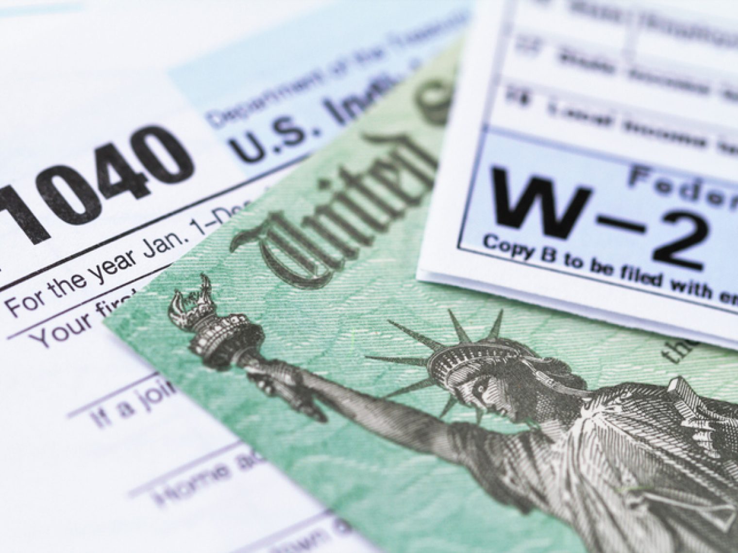 Close-up of a U.S. Form 1040 individual income tax return and a W-2 wage statement with a check from the IRS underneath.