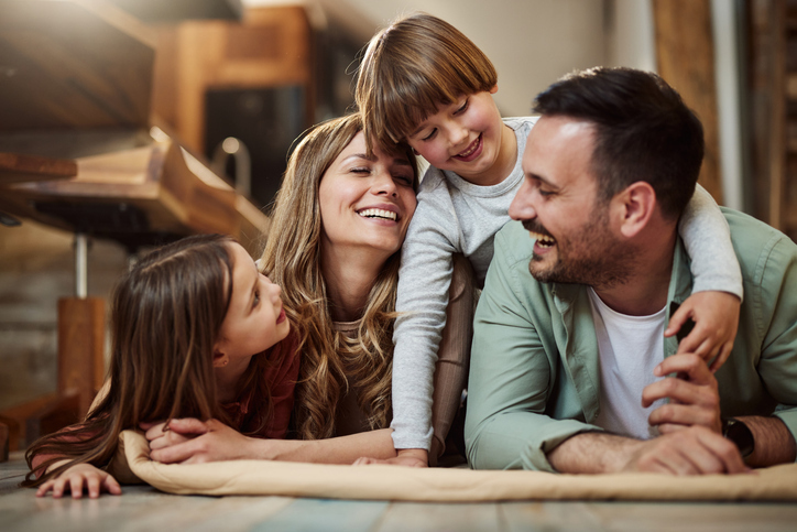 A happy family moment with a mother, father, and two children snuggling and laughing together in a cozy, indoor setting.