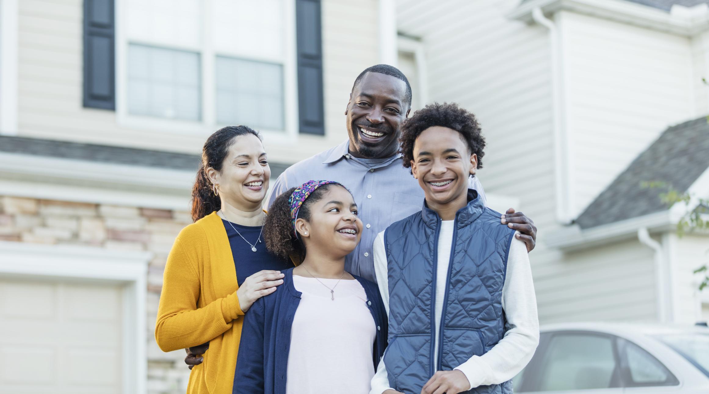 An African American family standing outside the new home they just bought.