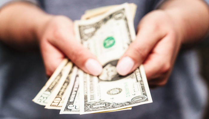 Close up of hands holding out US dollar bills.