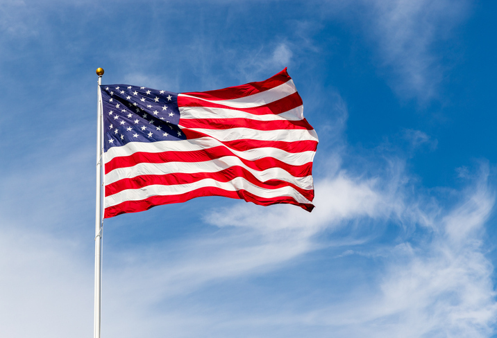 The United States flag is prominently displayed against a clear blue sky, waving in the wind on a bright day.