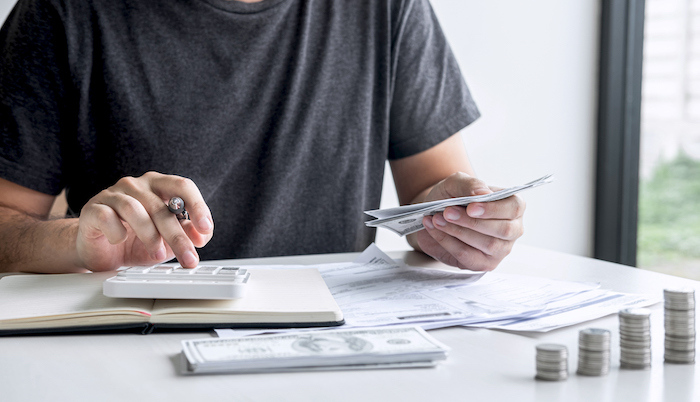 Slacked coin pile and man using calculator to calculating expenditure receipt bills of various activity cost and expenses.