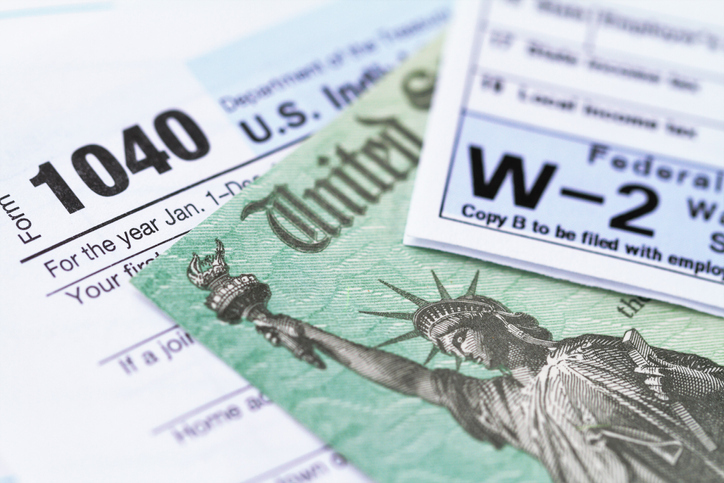 Close-up of a U.S. Form 1040 individual income tax return and a W-2 wage statement with a check from the IRS underneath.