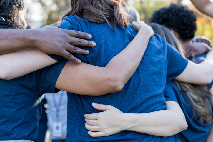 A close-up of a diverse group of people in blue shirts, embracing each other in a supportive huddle.